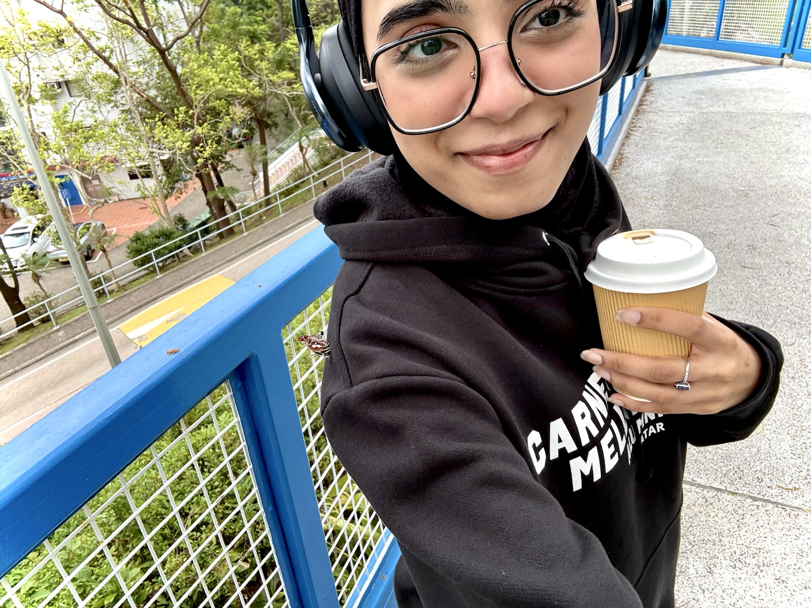 Eman holding a coffee with a butterfly resting on her shoulder